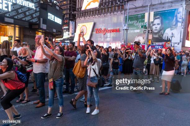 People stand on 42nd Street in Manhattan to photograph Manhattanhenge phenomenon when sun sets in alignment with streets run East to West.