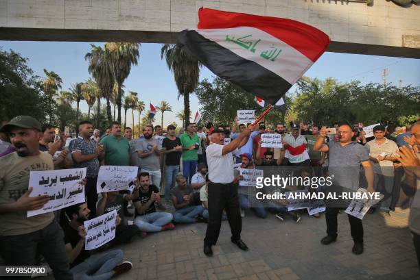 An Iraqi man waves a national flag as others shout slogans during a protest against poor services, unemployment and corruption as they gather in the...