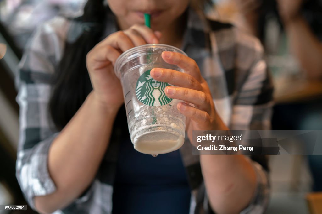 A girl drinks a Starbucks coffee with a plastic straw.