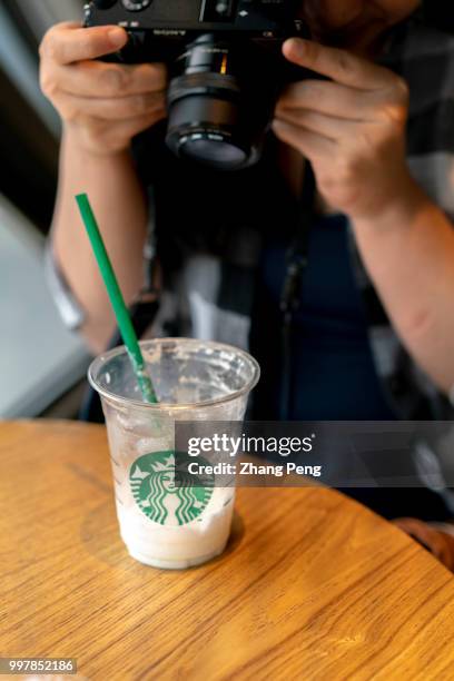 Girl is taking picture of a cup of Starbucks coffee, a plastic straw in it. Starbucks announced on July 9th that it would ban the use of plastic...