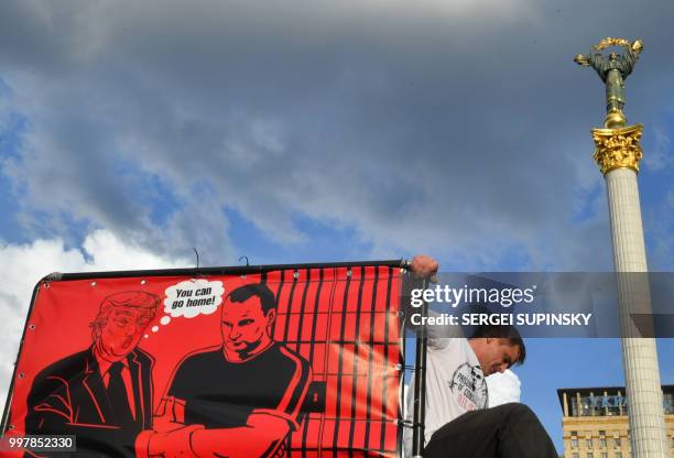 An activist sets a placard depicting US President Donald Trump speaking to Oleg Sentsov "You can go home!" during a rally at Independence Square in...