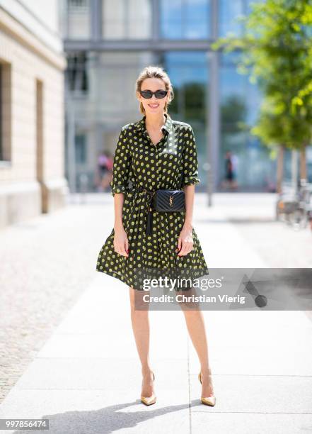 Alexandra Lapp is seen wearing a knee length dark green dress with green and yellow dots from Steffen Schraut, the Lou Belt Bag in black by Saint...