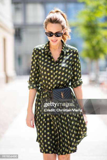 Alexandra Lapp is seen wearing a knee length dark green dress with green and yellow dots from Steffen Schraut, the Lou Belt Bag in black by Saint...