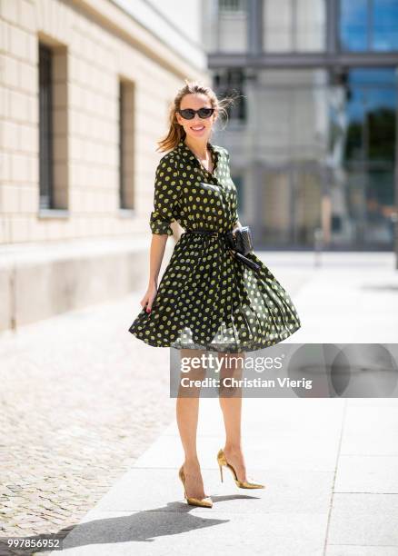 Alexandra Lapp is seen wearing a knee length dark green dress with green and yellow dots from Steffen Schraut, the Lou Belt Bag in black by Saint...