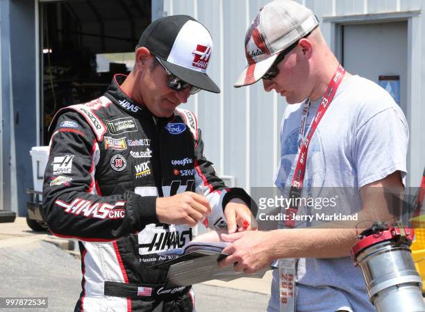 Clint Bowyer, driver of the Haas 30 Years of the VF1 Ford, signs an autograph in the garage area during practice for the Monster Energy NASCAR Cup...