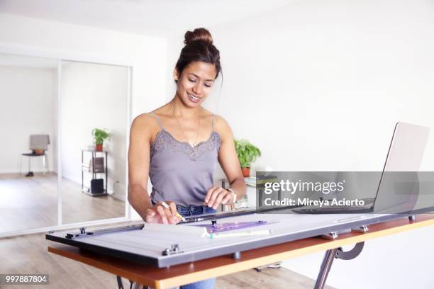 young ethnic woman drawing on her drafting table, with laptop nearby, in her studio - technophiler mensch stock-fotos und bilder