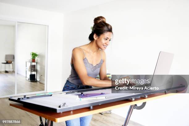 young ethnic woman working on her computer, on her drafting table, in her studio smiling - technophiler mensch stock-fotos und bilder