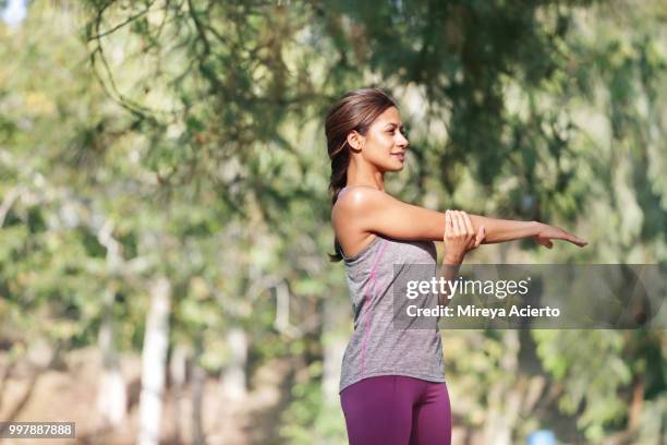 fit, ethnic woman stretches before a work out in a park in work out clothes. - mireya acierto stockfoto's en -beelden