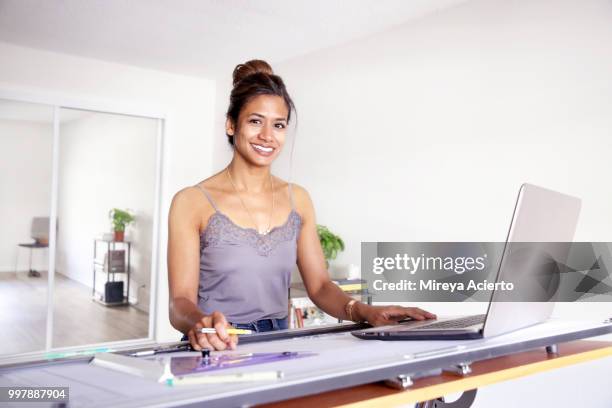 young ethnic woman smiling for the camera with her computer on her drafting table, in her studio smiling - technophiler mensch stock-fotos und bilder