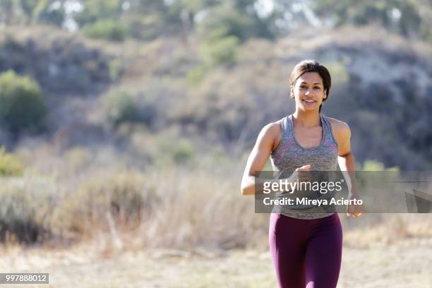 cropped image of fit, ethnic woman runs in a field of grass in a park in work out clothes - mireya acierto stockfoto's en -beelden