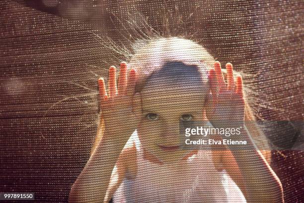 girl with static hair looking through safety netting of a trampoline - hair standing on end stock pictures, royalty-free photos & images