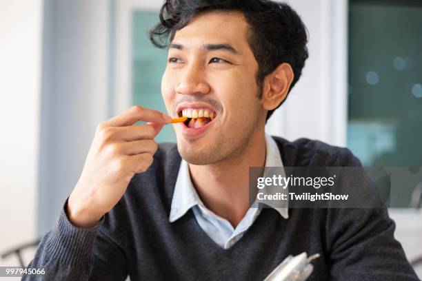 one young college students adult male taking a break sat eating snack with happiness - snack break stock pictures, royalty-free photos & images