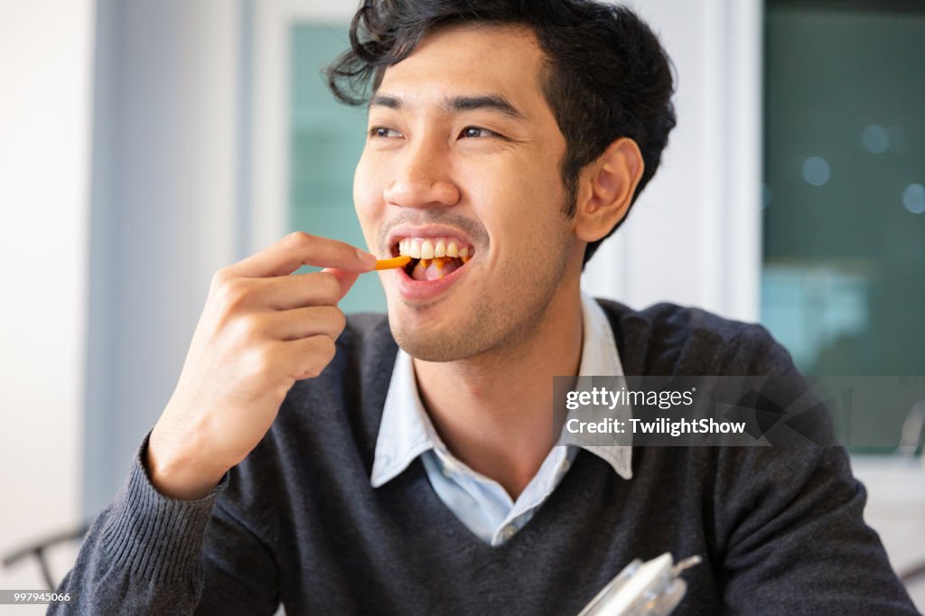 一個年輕的大學生成年男性休息坐在吃零食與幸福