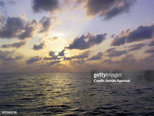 sunset through the clouds over the water of the arabian sea off - agarwal stock pictures, royalty-free photos & images