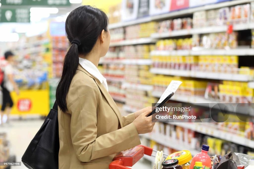 Woman holding smart phone with shopping list in supermarket