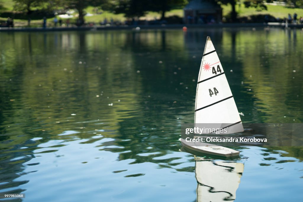 Miniature remote-controlled sail boat on the surface of a pond during a sunny day.