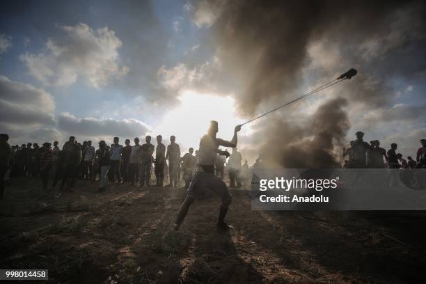 Palestinian throws rock with a slingshot as Israeli forces use tear gas to disperse Palestinian demonstrators taking part in the "Great March of...