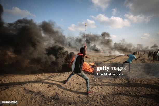 Palestinian throws rock with a slingshot as Israeli forces use tear gas to disperse Palestinian demonstrators taking part in the "Great March of...