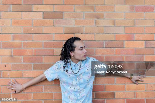 portrait of a young man standing alone in front of a brick wall - micah stock pictures, royalty-free photos & images