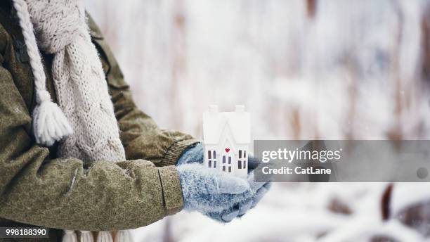 female hands holding tiny home in snowy weather - winter house stock pictures, royalty-free photos & images