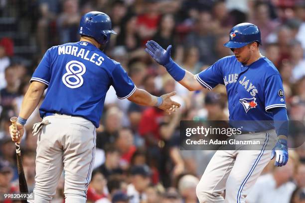 Justin Smoak high fives Kendrys Morales of the Toronto Blue Jays after scoring in the third inning of a game against the Boston Red Sox at Fenway...