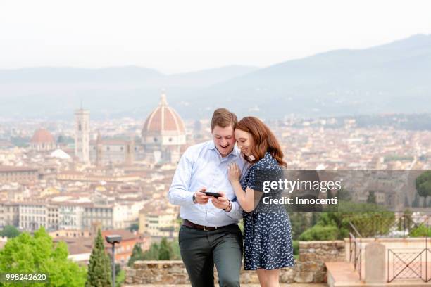 young couple smiling at mobile phone, santa maria del fiore in background, florence, toscana, italy - mimosa fiore fotografías e imágenes de stock