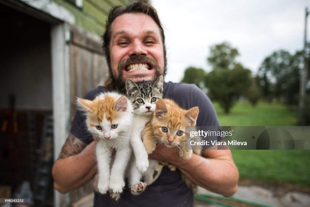 Man grinning with three kittens in arms