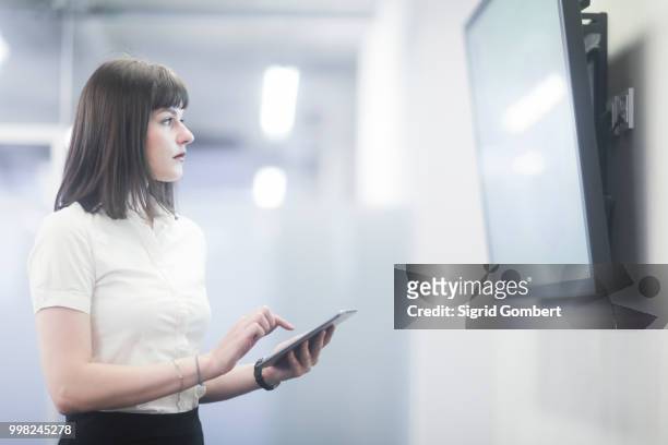 businesswoman using digital tablet looking at tv - sigrid gombert stock pictures, royalty-free photos & images