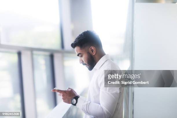 young man using mobile phone in office - sigrid gombert photos et images de collection