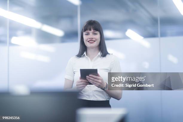 businesswoman using digital tablet, looking at camera smiling - sigrid gombert stock-fotos und bilder