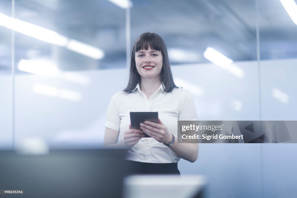 Businesswoman using digital tablet, looking at camera smiling