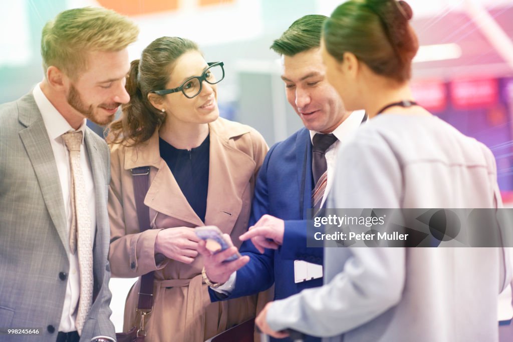 Group of businessmen and women standing, catching up, businessman looking at smartphone