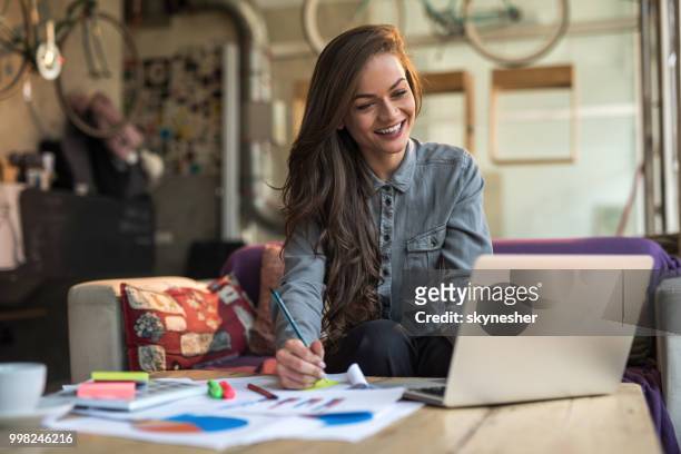 junge glücklich geschäftsfrau notizen während der arbeit am laptop in einem café. - skynesher stock-fotos und bilder
