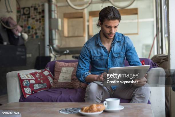 junger mann in einem café entspannen und lesen einer e-mail auf einem computer. - skynesher stock-fotos und bilder