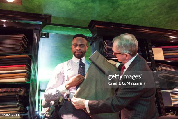 senior tailor assisting young male customer in traditional tailors shop - tailor stock pictures, royalty-free photos & images