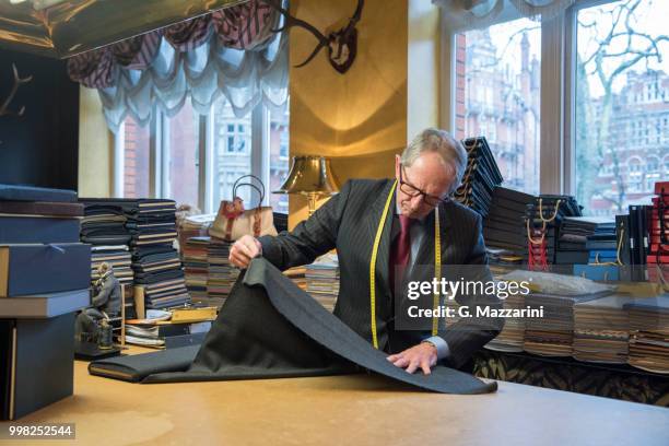 tailor examining roll of cloth in tailor shop - sastre fotografías e imágenes de stock