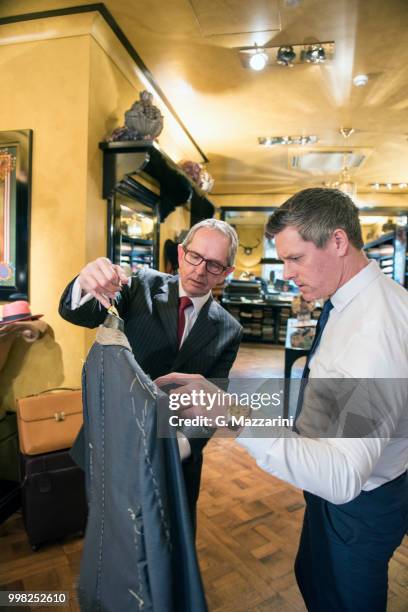 tailor showing customer bespoke jacket in tailors shop - custom tailored suit stock pictures, royalty-free photos & images