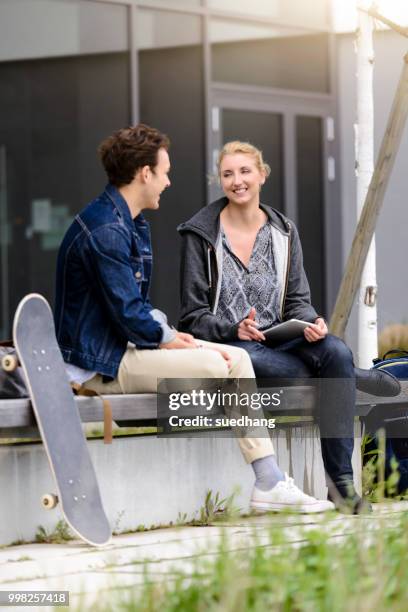 young male and female students sitting chatting on wall outside college - munich university stock pictures, royalty-free photos & images