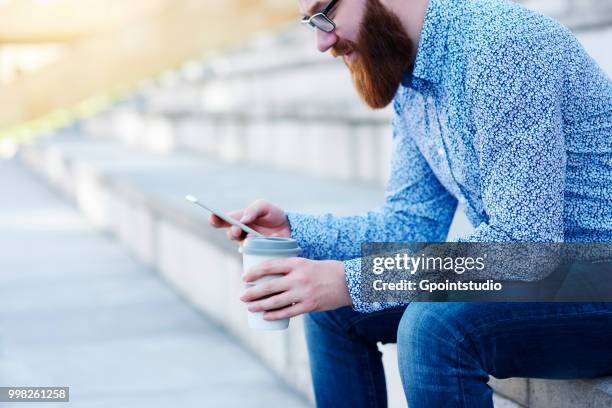 bearded man sitting on step using smartphone - gpointstudio imagens e fotografias de stock