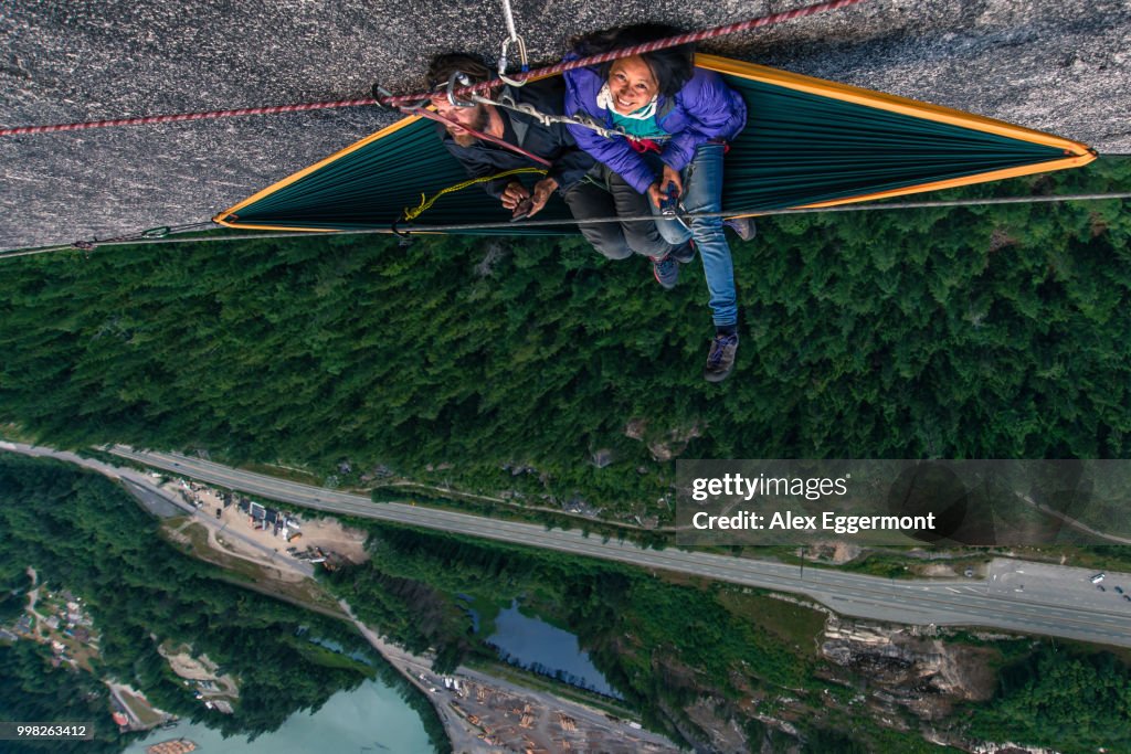 Man and woman sitting on hammock on bellygood ledge, The Chief, Squamish, Canada, overhead portrait