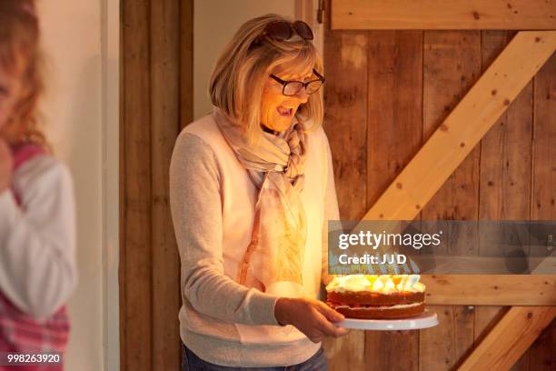 senior woman carrying birthday cake with lit candles in kitchen - holding birthday cake stock pictures, royalty-free photos & images