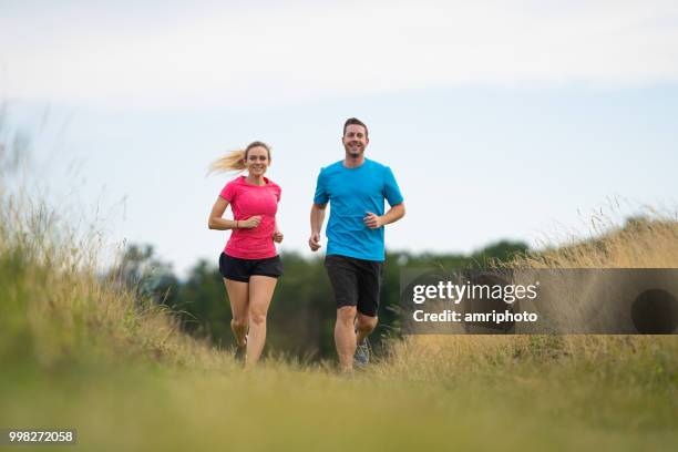 couple jogging together on meadow in summer - couple exercising 30s stock pictures, royalty-free photos & images