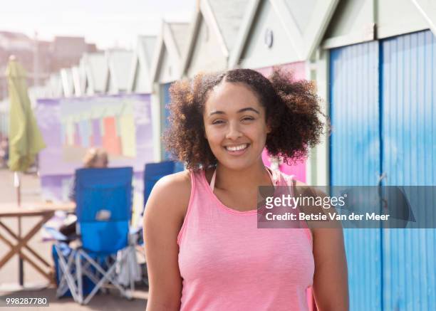 mixed race woman standing in front of row of colorful beach huts. - meer photos et images de collection