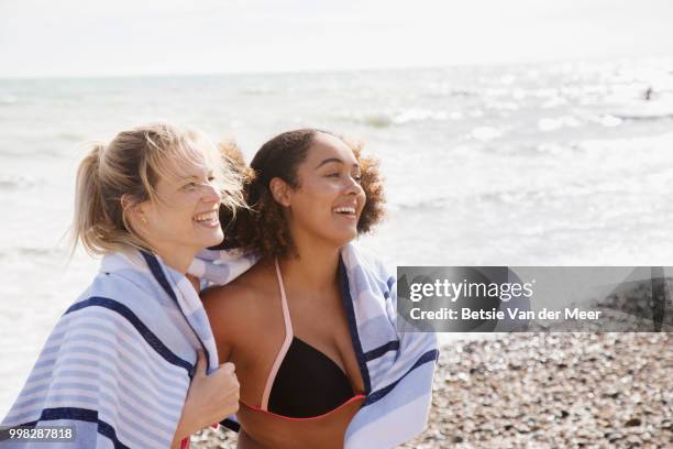 women wrapped in towel standing on beach, laughing. - meer photos et images de collection