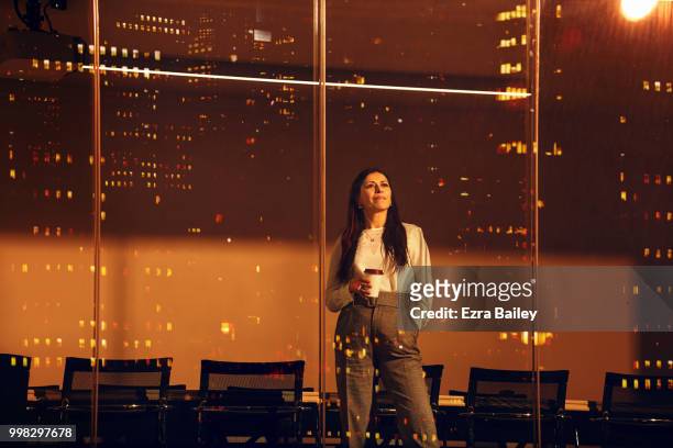 Portrait of a business woman looking out of a modern high rise office window at night.