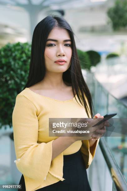 若いアジアの女性は、彼女の携帯電話をチェックしながら、バルコニーに立っています。 - vanguardians ストックフォトと画像