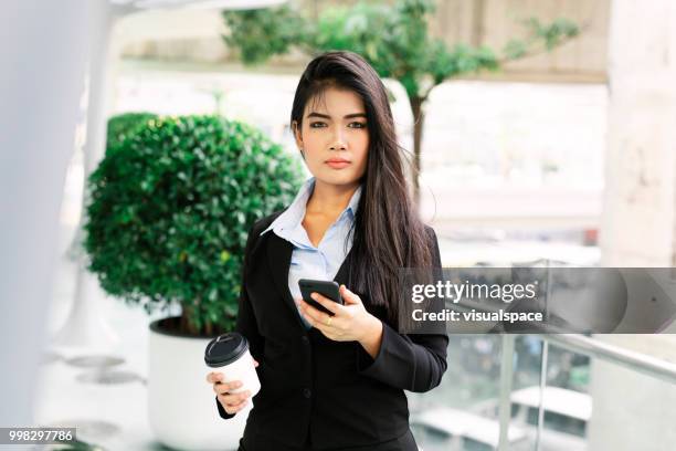 junge asiatische frau, stehend auf einem balkon während der überprüfung ihr handy. - vanguardians stock-fotos und bilder