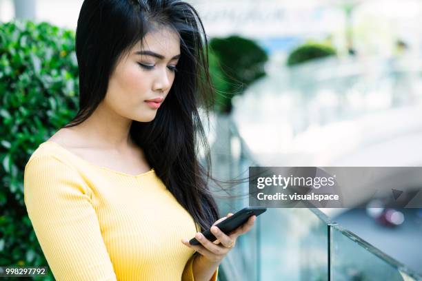 年輕的亞洲婦女站在陽臺上, 同時檢查她的電話。 - vanguardians 個照片及圖片檔