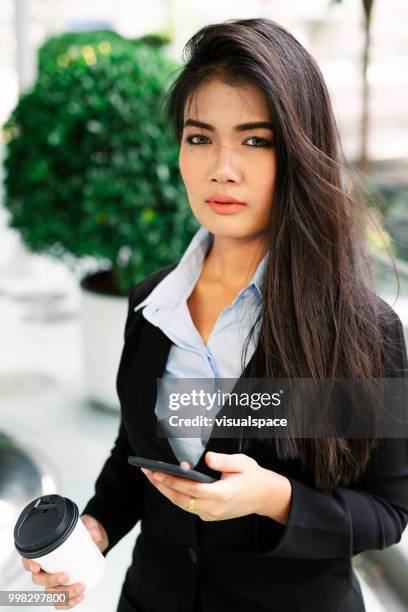 junge asiatische frau, stehend auf einem balkon während der überprüfung ihr handy. - vanguardians stock-fotos und bilder