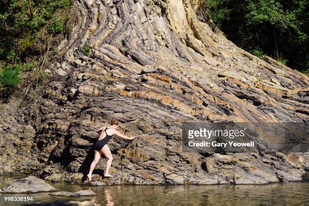 woman climbing over rocks by a secluded lake - yeowell imagens e fotografias de stock